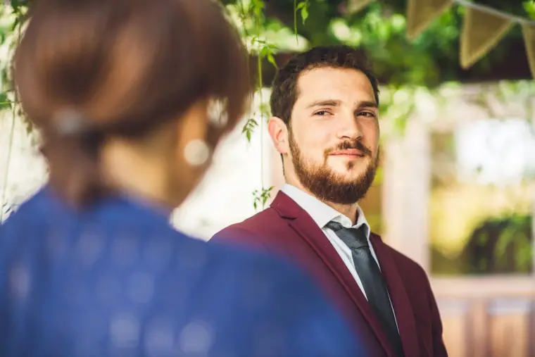 Groom smiling during the outdoor ceremony, a guest in blue blurred in the foreground