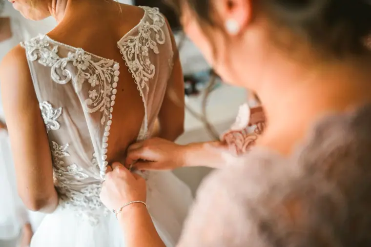 Bridesmaid fastening the buttons on the bride's lace-backed gown