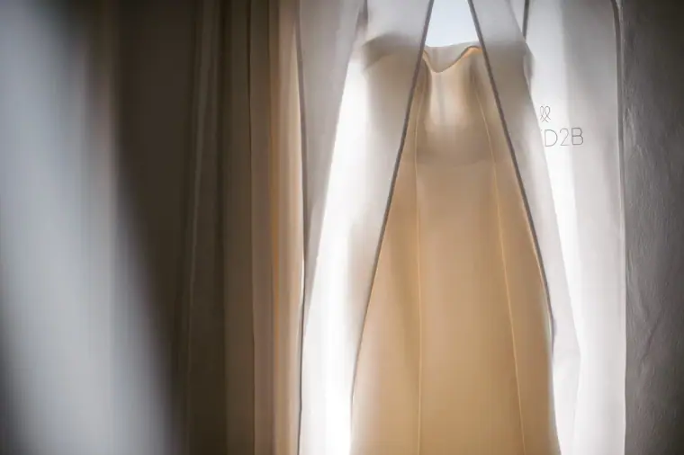 Wedding dress hanging in a garment bag against a curtained window