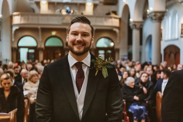 Smiling groom waiting in the church as guests fill the pews behind him