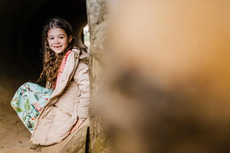 Young girl in a pink coat smiling beside a wooden post
