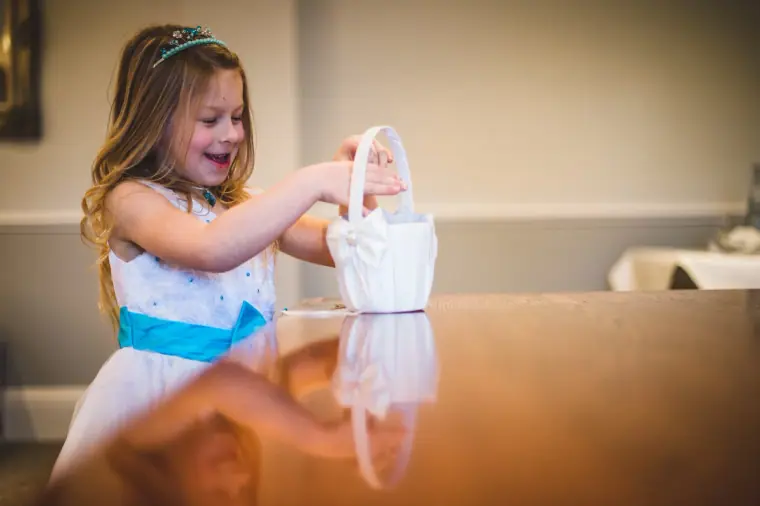 Flower girl in a white dress with a blue sash holding a petal basket