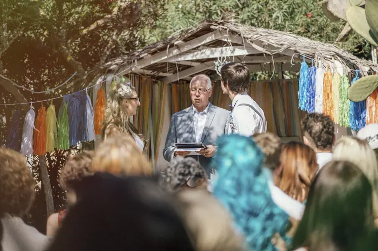 Guests watching the ceremony under a thatched shelter hung with rainbow tassels