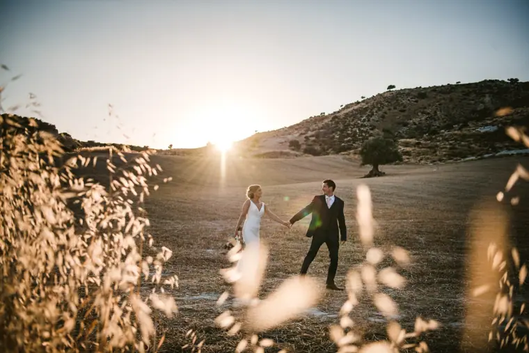 Bride and groom walking through a sunlit valley, framed by wild grasses