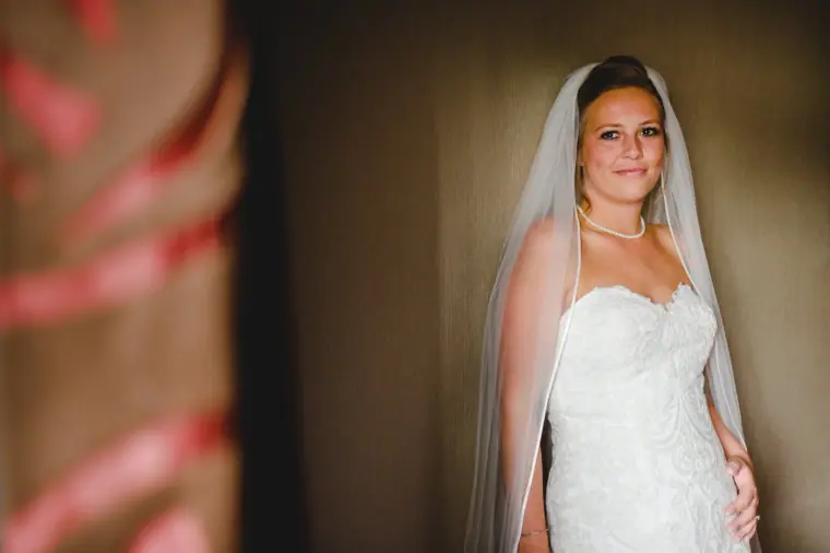 Bride standing in her veil and lace gown by a doorway