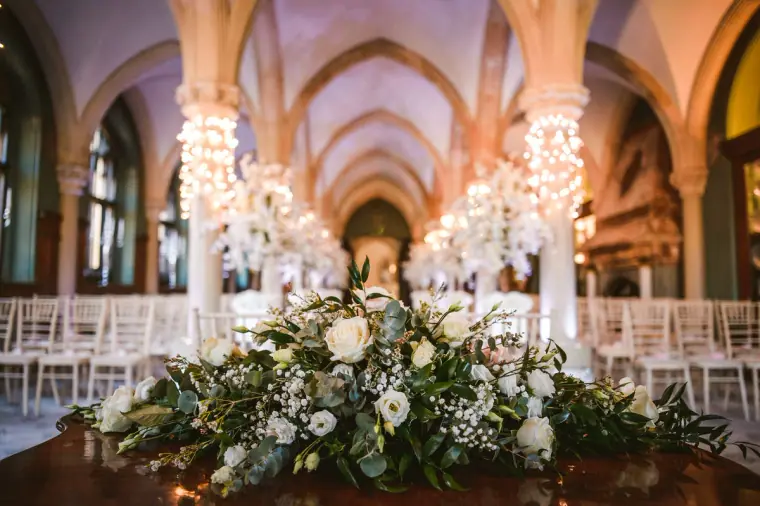 White rose and greenery arrangement before rows of ceremony chairs under gothic arches