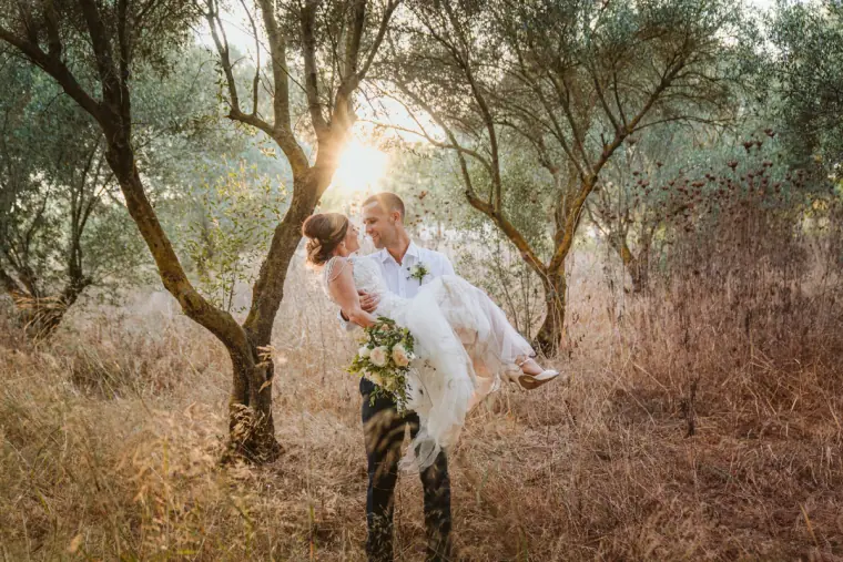 Groom lifting his bride among olive trees in golden backlight