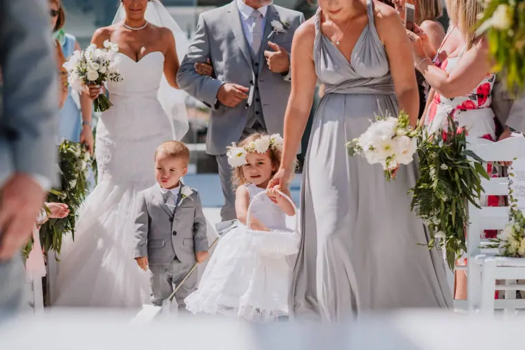 Bridesmaids in grey gowns, a pageboy and a flower girl walking down the aisle