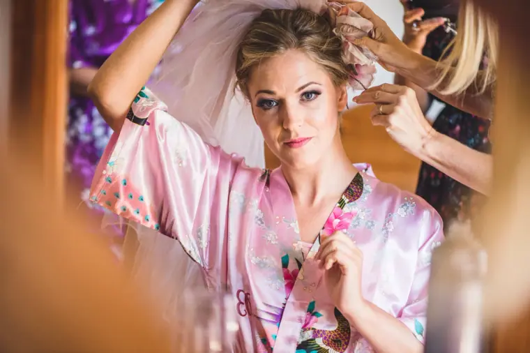 Bride in a pink floral robe as her hair is finished, framed by a doorway