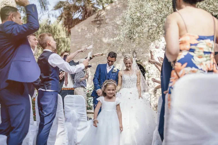 Newlyweds walking out through petal-throwing guests with a flower girl