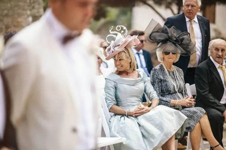 Groom waiting at the front as guests in fascinators sit in the courtyard