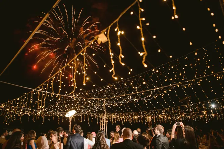 Fireworks bursting above a fairy-lit canopy over the evening party