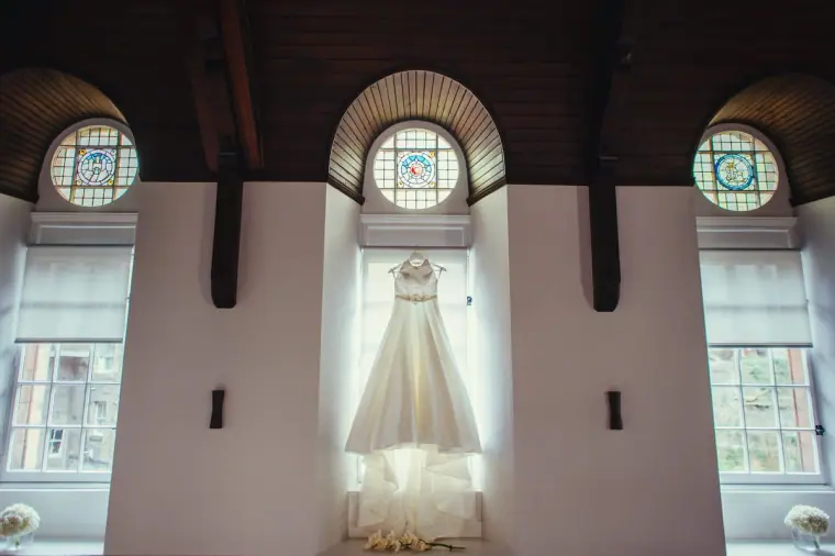 Wedding dress hanging beneath arched stained-glass windows