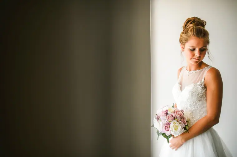 Bride holding her bouquet and looking down in soft window light