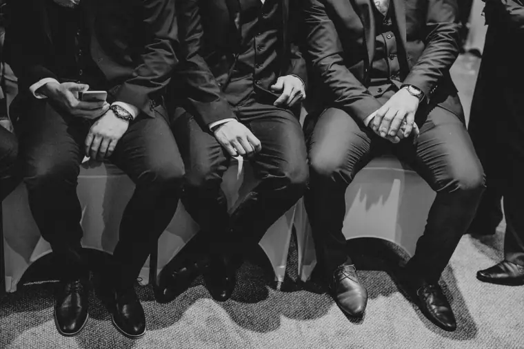Black-and-white close-up of the groomsmen's polished shoes and knees as they sit