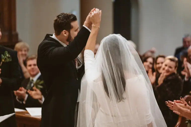 Groom punching the air in celebration beside the veiled bride as guests applaud