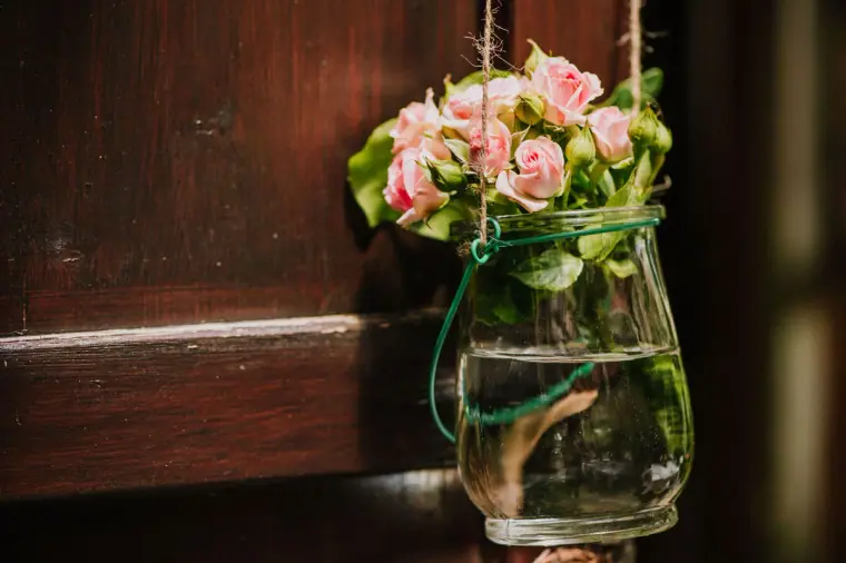 Hanging glass jar of pink roses on a rustic wooden door