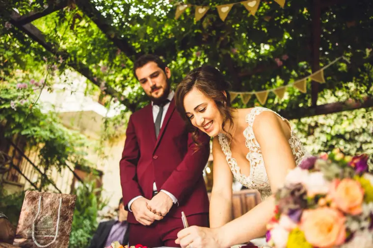 Groom signing the register as the bride laughs beside a colourful bouquet
