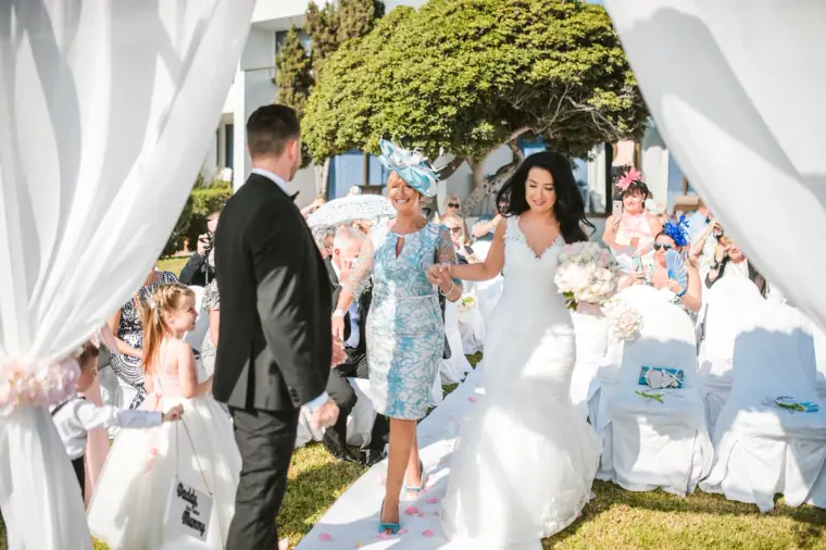 Jaclyn walked down the aisle by a woman in blue as Steven waits under the canopy