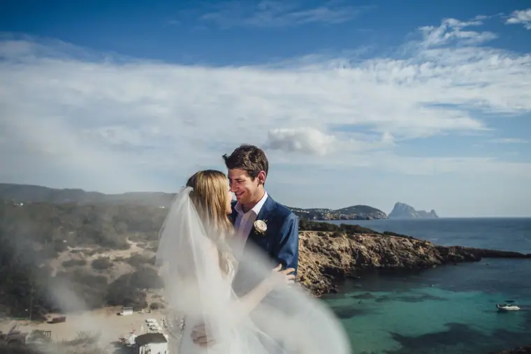 Groom kissing his bride above a cove as her veil blows in the wind