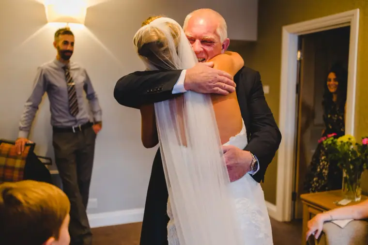 Bride hugging her father in the suite as others watch