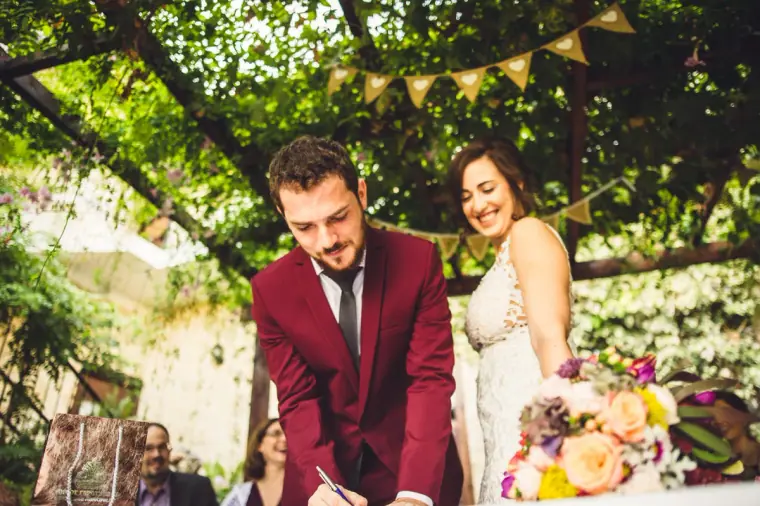 Madeliene and Itai signing the marriage register under the bunting-strung pergola