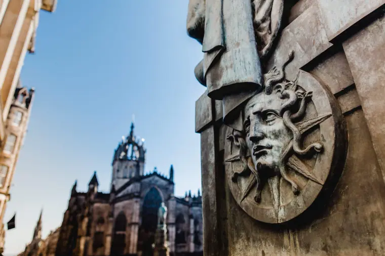 St Giles' Cathedral crown spire beside a bronze sculpted face on the Royal Mile