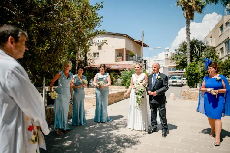 Bride and her father arriving at Ayia Kyriaki as bridesmaids in blue wait