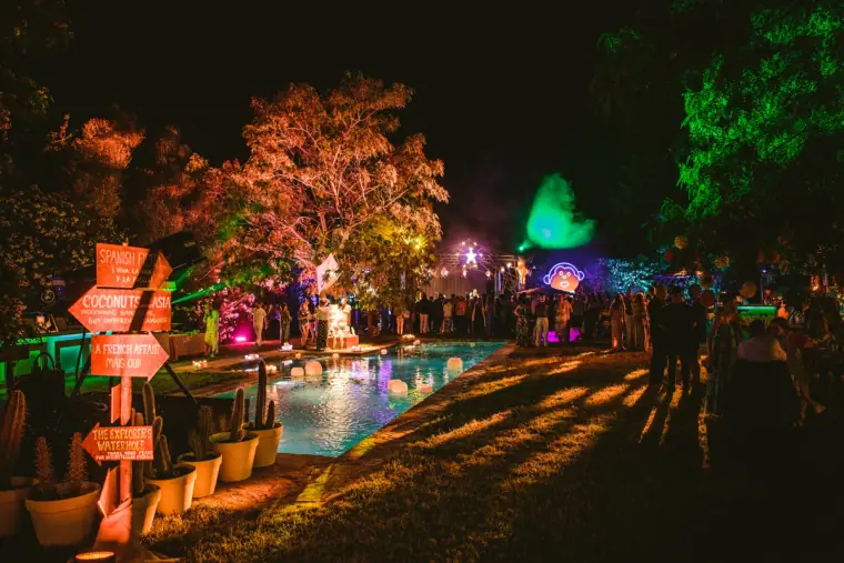 Garden pool surrounded by colourful lights and wooden signposts at night