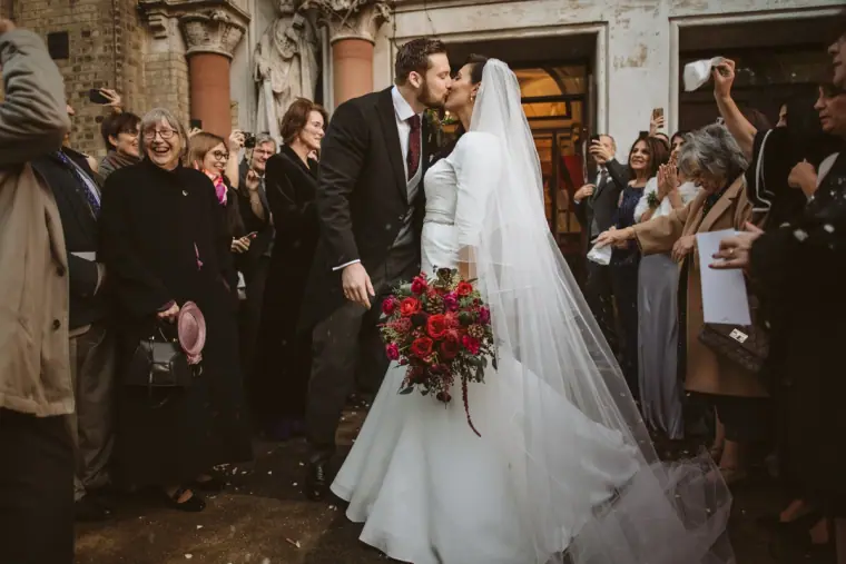 Bride and groom kissing at the church door as guests throw rice
