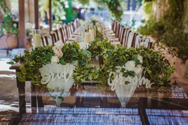 Top table with ivy and white flowers and acrylic "bride" and "groom" chair signs