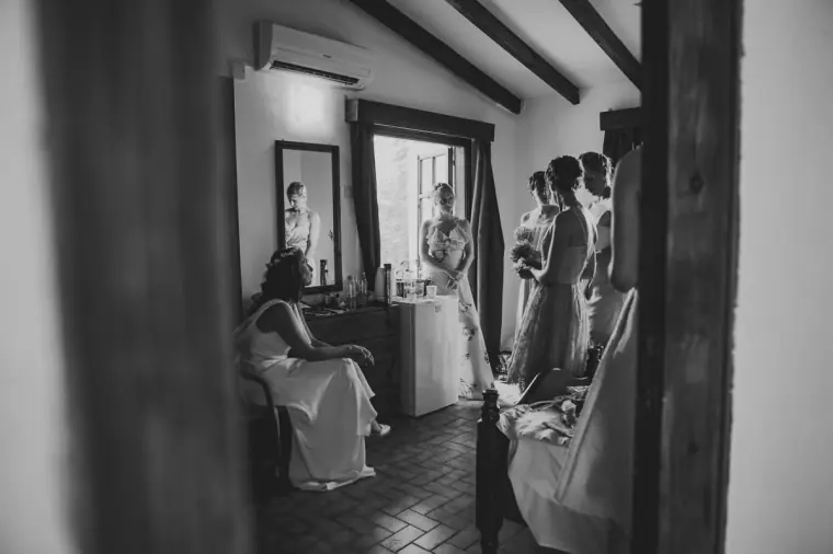 Black-and-white photo of bridesmaids gathering in a beamed corridor with the bride