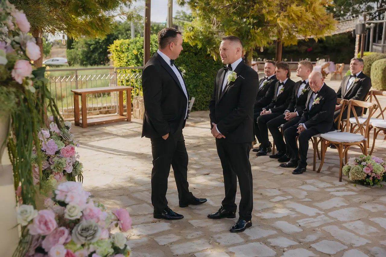 Oliver and a groomsman waiting beside the floral arch at Liopetro