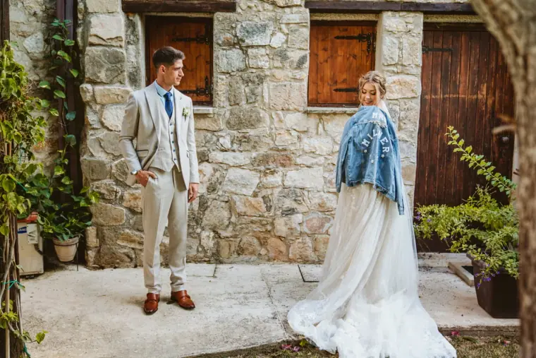 Bride in a customised denim jacket and groom posing by the inn's stone wall