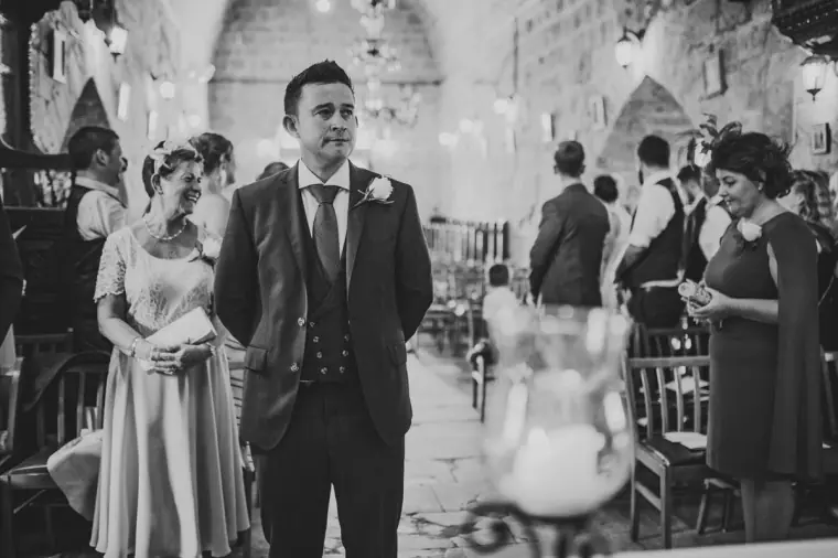 Black-and-white photo of the groom turning to see his bride walk down the aisle