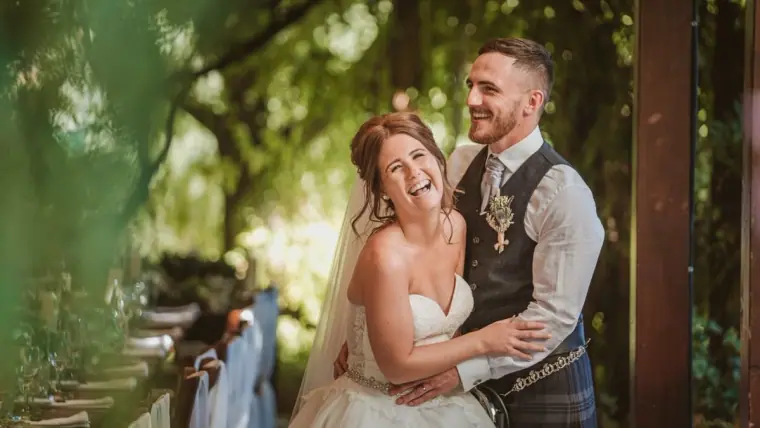 Hannah laughing in Keith's arms beneath trees with a ribbon-tied chair beside them