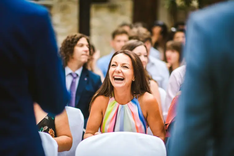 Wedding guest in a striped dress laughing as she takes her seat for the ceremony