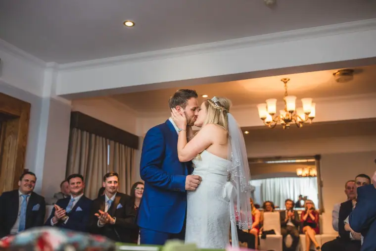 Newlyweds sharing their first kiss as guests applaud in the ceremony room