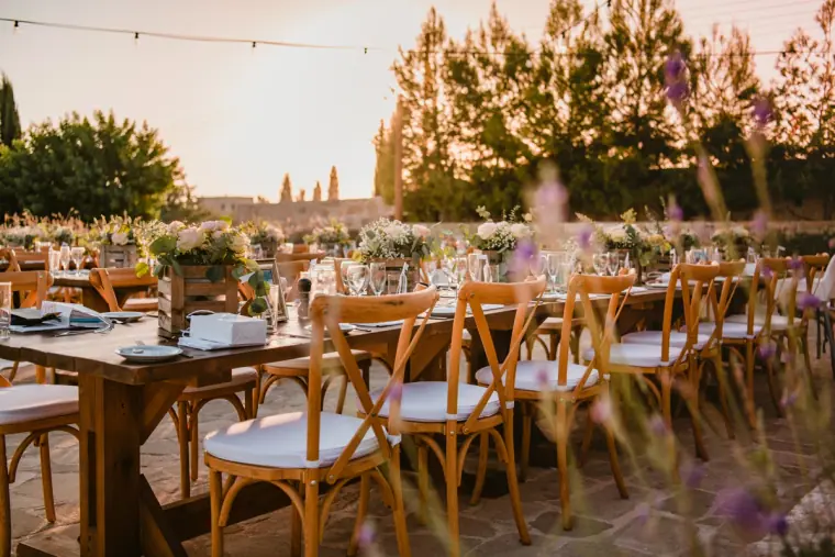 Long wooden tables with cross-back chairs and flowers in golden evening light
