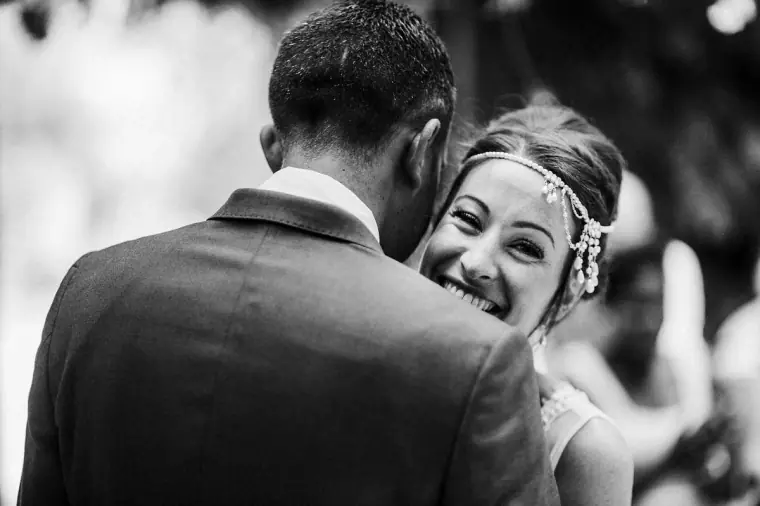 Black-and-white photo of the bride beaming as she hugs the groom