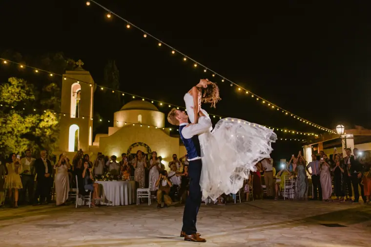 Groom lifting the bride on the dance floor under festoon lights by a lit church