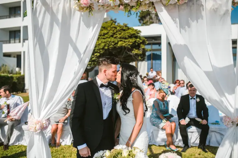 Jaclyn and Steven kissing at the flower-topped canopy as guests look on