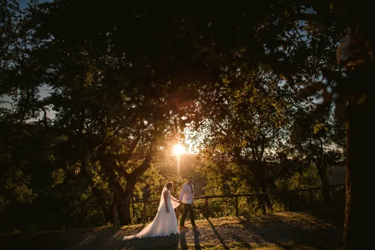 Couple silhouetted by a sunburst through dark woodland at sunset