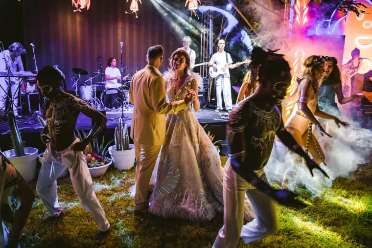 Couple dancing among costumed performers and smoke beneath stage lights