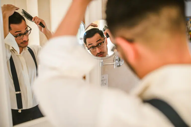 Groomsmen in braces adjusting their shirts in front of a mirror