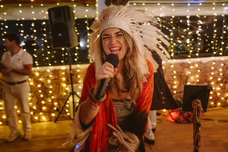 Singer in a feathered headdress performing in front of fairy lights at night