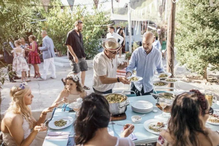 Guests serving themselves at a long outdoor table of shared dishes
