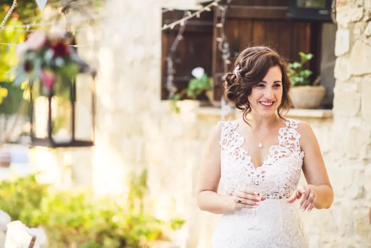 Bride in a lace V-neck gown smiling in the sunlit courtyard
