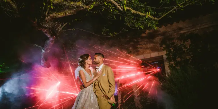 Couple embracing among red laser beams in a dark garden