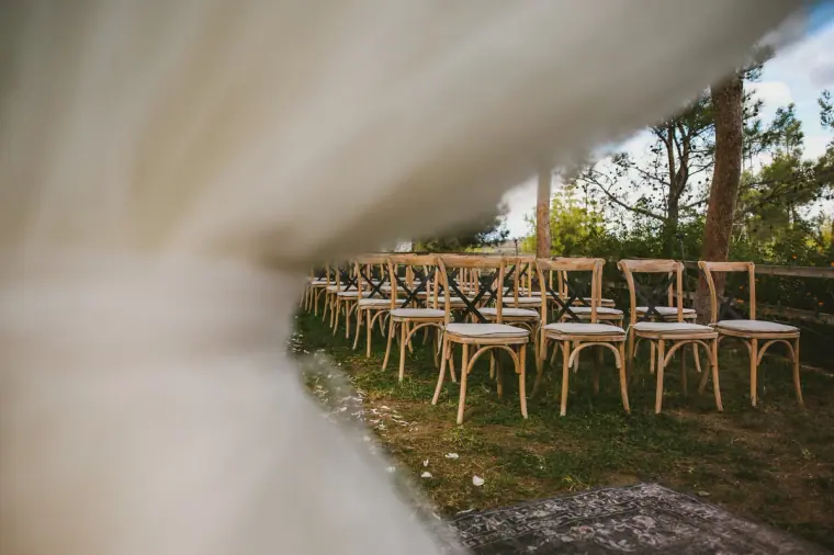 Rows of wooden cross-back ceremony chairs framed by white drapery